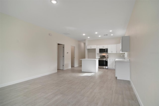 kitchen with appliances with stainless steel finishes, white cabinetry, sink, a kitchen island, and light hardwood / wood-style flooring