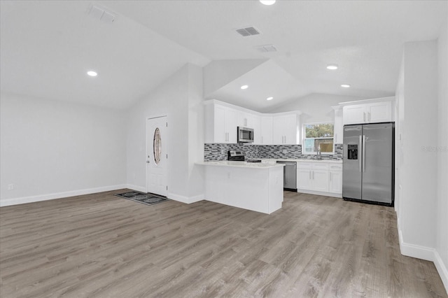 kitchen featuring kitchen peninsula, vaulted ceiling, stainless steel appliances, light wood-type flooring, and white cabinetry