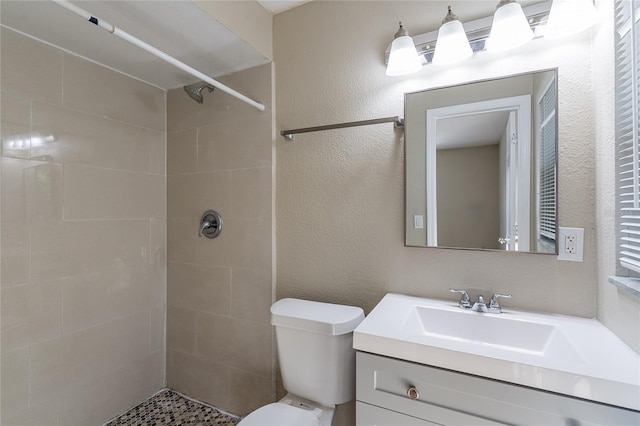 bathroom featuring toilet, tiled shower, and vanity