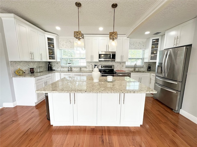 kitchen with appliances with stainless steel finishes, a center island, white cabinetry, sink, and hanging light fixtures