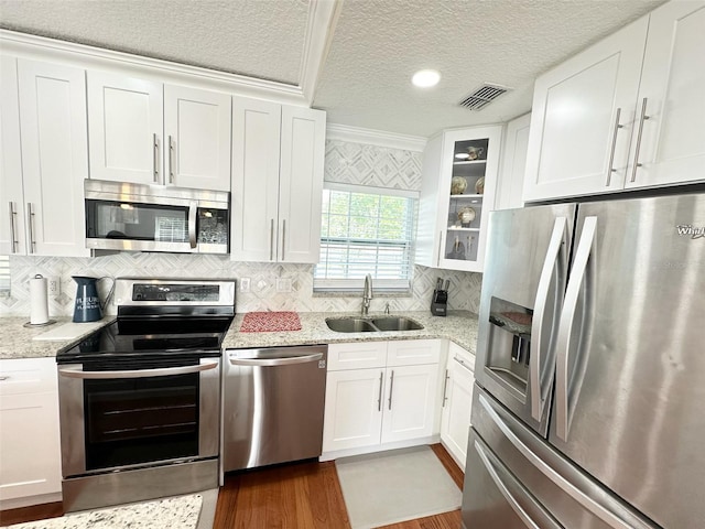 kitchen featuring white cabinetry, stainless steel appliances, ornamental molding, light stone counters, and sink