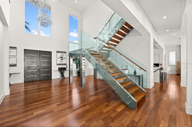 entrance foyer featuring crown molding, wood-type flooring, a towering ceiling, and an inviting chandelier