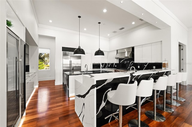 kitchen featuring wall chimney range hood, decorative backsplash, white cabinets, a kitchen bar, and decorative light fixtures