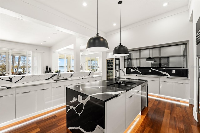 kitchen featuring tasteful backsplash, hanging light fixtures, a center island with sink, and white cabinets