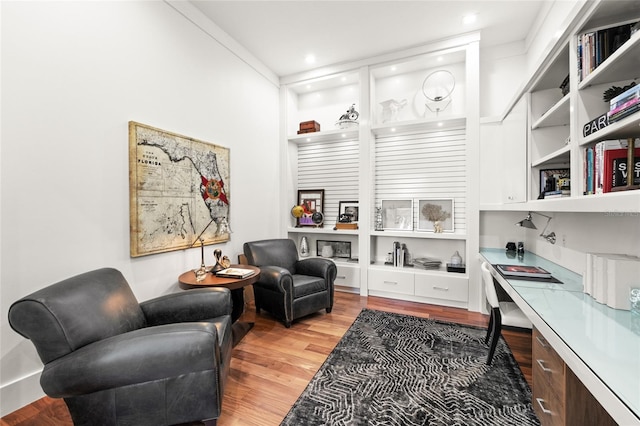 sitting room featuring crown molding, built in desk, and light hardwood / wood-style flooring