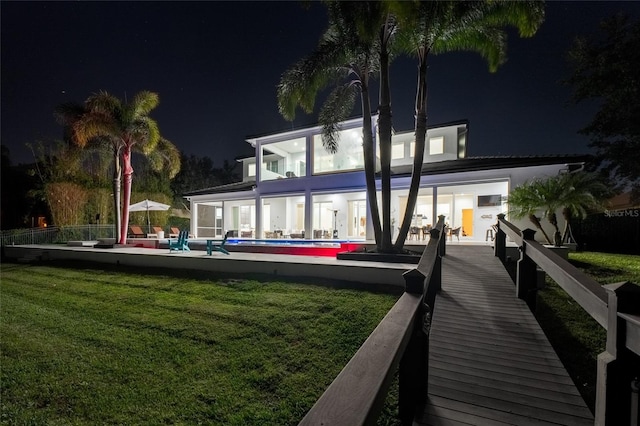 back house at twilight featuring a fenced in pool, a lawn, and a patio