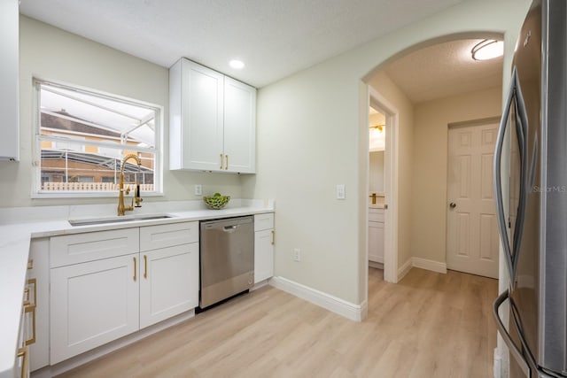 kitchen with sink, white cabinetry, light wood-type flooring, appliances with stainless steel finishes, and a textured ceiling