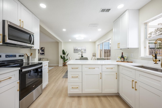 kitchen featuring white cabinets, appliances with stainless steel finishes, light hardwood / wood-style flooring, and kitchen peninsula