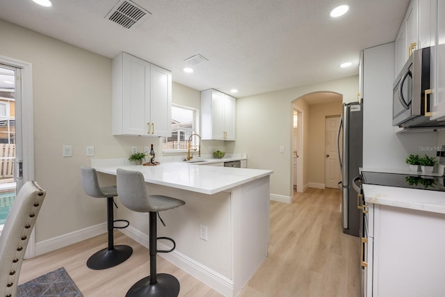 kitchen with a kitchen bar, kitchen peninsula, appliances with stainless steel finishes, light wood-type flooring, and white cabinets