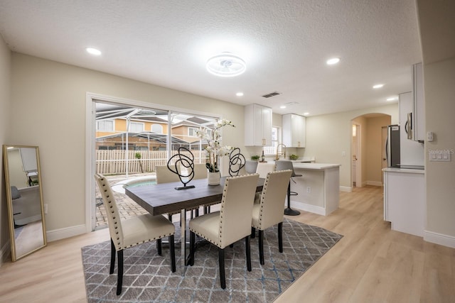 dining room featuring sink, a textured ceiling, and light hardwood / wood-style flooring