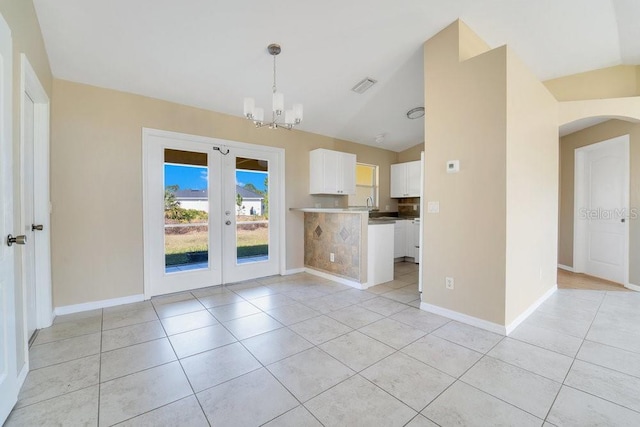 unfurnished living room featuring french doors, a notable chandelier, lofted ceiling, and light tile patterned flooring