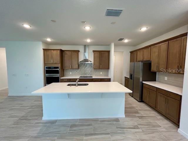 kitchen with stainless steel appliances, a center island with sink, wall chimney range hood, tasteful backsplash, and sink