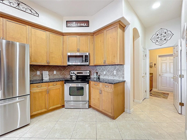 kitchen featuring dark stone counters, backsplash, light tile patterned floors, and stainless steel appliances