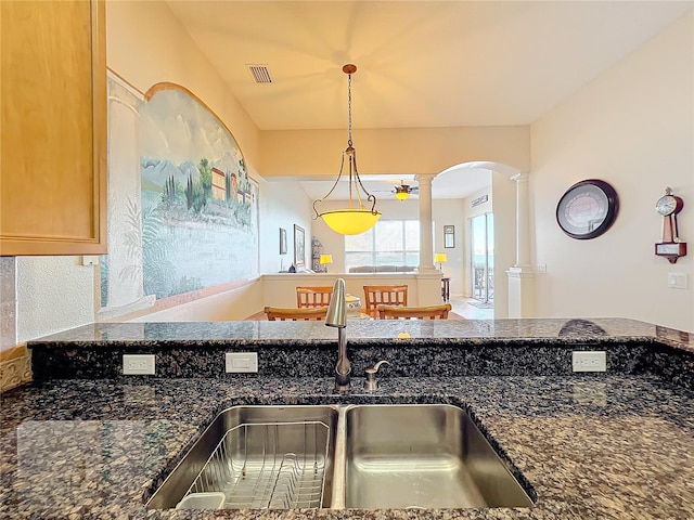 kitchen featuring decorative columns, dark stone countertops, sink, and pendant lighting