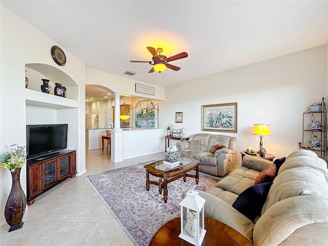 tiled living room featuring built in shelves, ceiling fan, and ornate columns