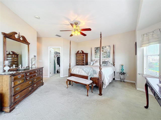 bedroom with ceiling fan, a walk in closet, light carpet, and a closet