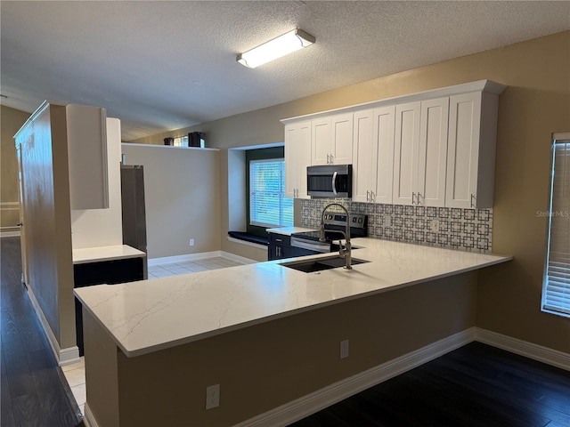 kitchen featuring stainless steel appliances, kitchen peninsula, a textured ceiling, decorative backsplash, and white cabinets