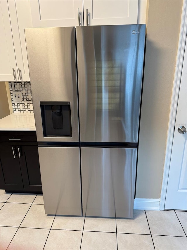 kitchen with stainless steel fridge with ice dispenser, light stone counters, light tile patterned flooring, backsplash, and white cabinets