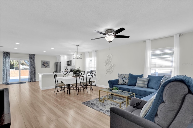 living room featuring a textured ceiling, ceiling fan with notable chandelier, light hardwood / wood-style flooring, and a wealth of natural light