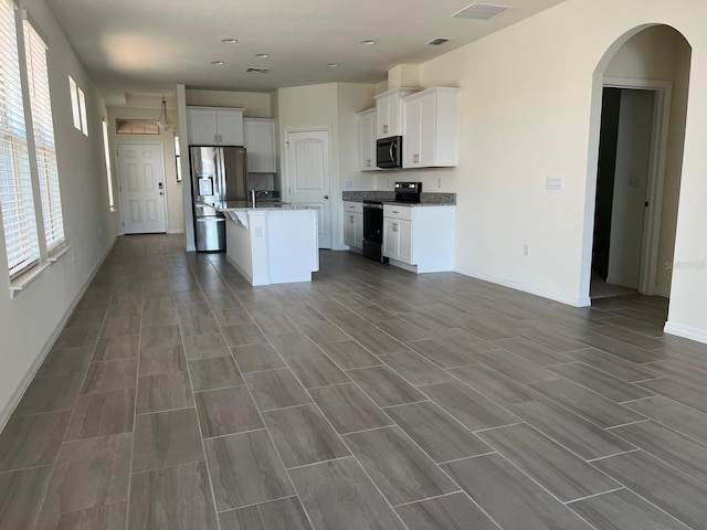 kitchen with electric range, a kitchen island with sink, plenty of natural light, and stainless steel fridge