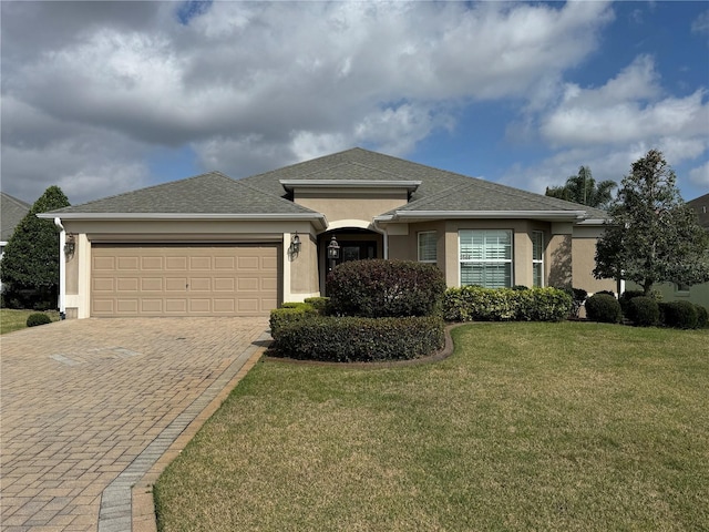 view of front facade featuring decorative driveway, roof with shingles, stucco siding, a front yard, and a garage