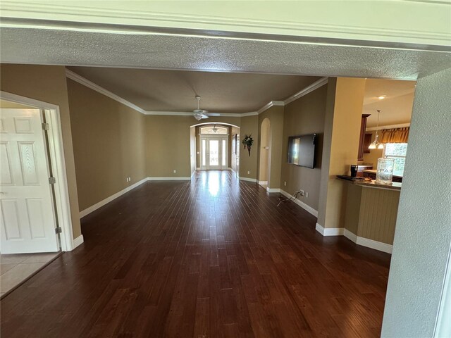 unfurnished living room with ceiling fan, ornamental molding, arched walkways, and dark wood-type flooring