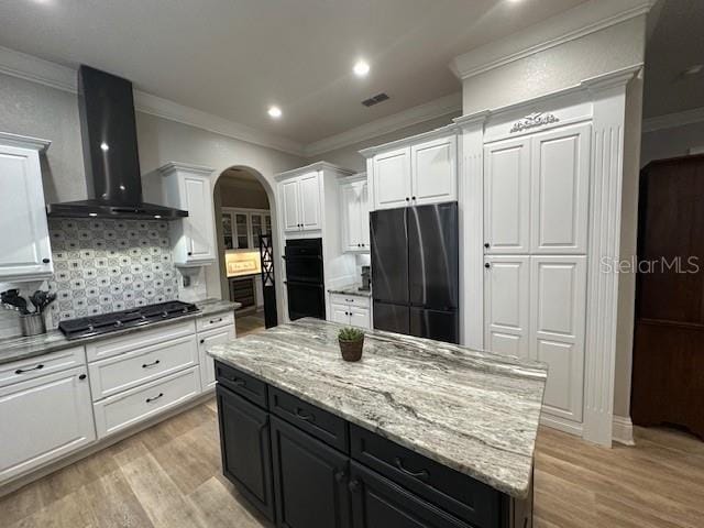 kitchen with a center island, wall chimney exhaust hood, backsplash, refrigerator, and stainless steel gas stovetop