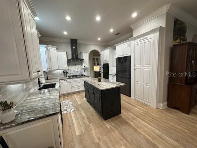 kitchen with white cabinetry, a center island, sink, wall chimney range hood, and decorative backsplash