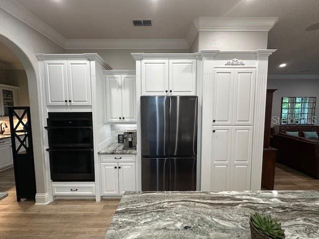 kitchen with double oven, light stone countertops, white cabinetry, and stainless steel refrigerator