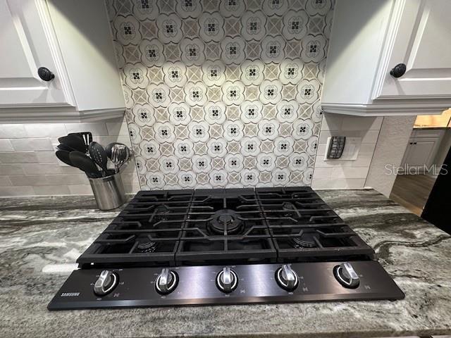 interior details with decorative backsplash, light stone counters, white cabinetry, and black gas cooktop