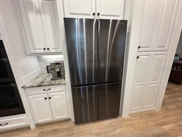 kitchen with white cabinets, light hardwood / wood-style floors, stainless steel refrigerator, and light stone counters