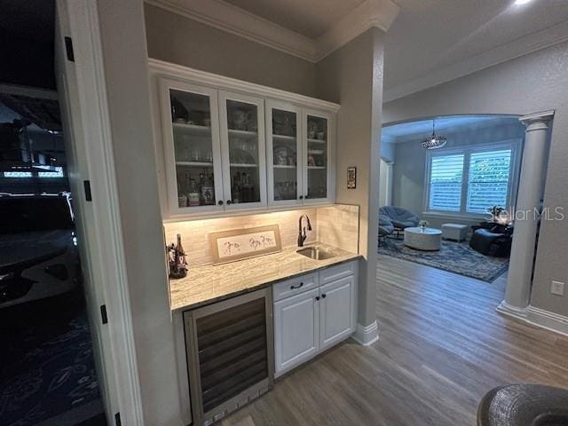 bar featuring decorative backsplash, ornamental molding, beverage cooler, sink, and white cabinets