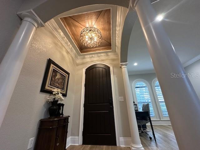 foyer with hardwood / wood-style floors, an inviting chandelier, ornate columns, and crown molding