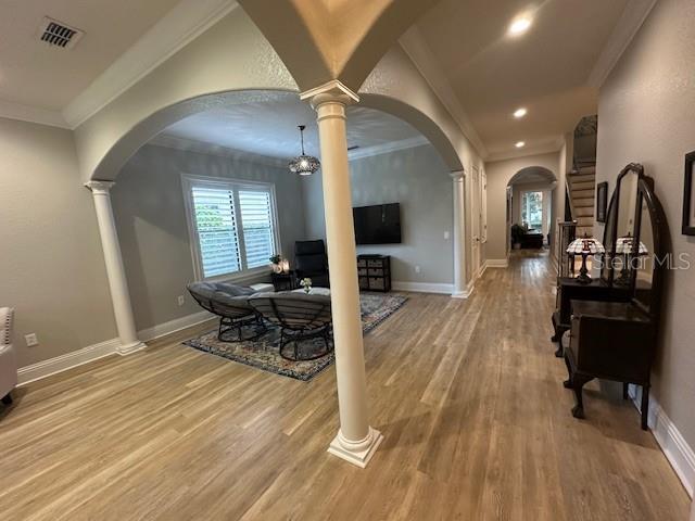 interior space featuring a chandelier, hardwood / wood-style flooring, decorative columns, and ornamental molding