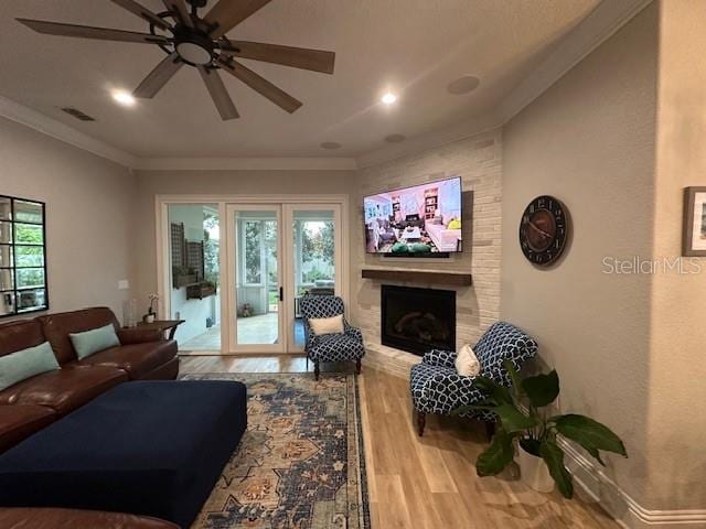 living room with ceiling fan, light wood-type flooring, a fireplace, and ornamental molding