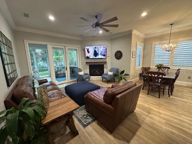 living room featuring light hardwood / wood-style floors, ceiling fan with notable chandelier, and ornamental molding