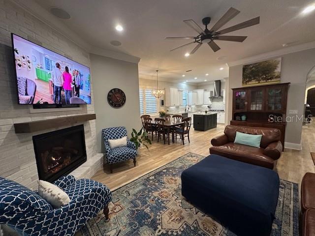 living room with a fireplace, crown molding, light hardwood / wood-style flooring, and ceiling fan with notable chandelier