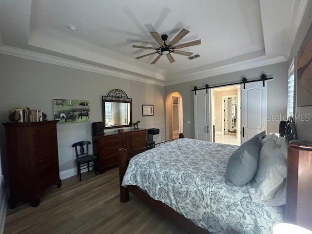 bedroom featuring hardwood / wood-style floors, a barn door, a tray ceiling, and ceiling fan