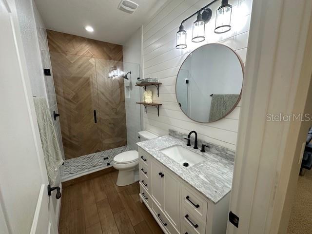 bathroom with a tile shower, vanity, hardwood / wood-style flooring, and toilet