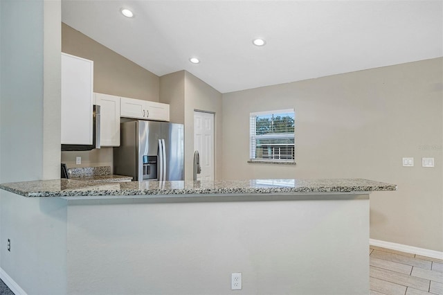 kitchen featuring light stone counters, kitchen peninsula, stainless steel fridge, and white cabinets