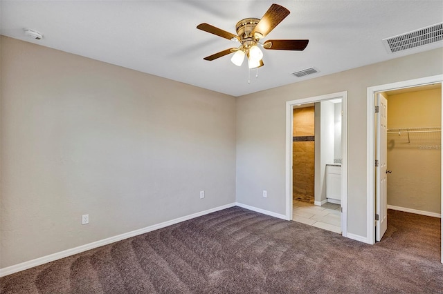 unfurnished bedroom featuring a walk in closet, a closet, ceiling fan, and light colored carpet