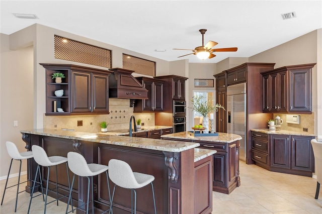 kitchen with appliances with stainless steel finishes, dark brown cabinetry, kitchen peninsula, and custom exhaust hood