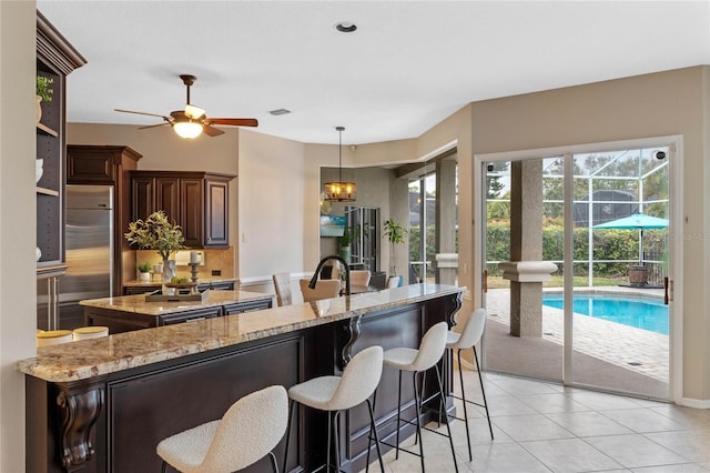 kitchen featuring built in fridge, decorative light fixtures, ceiling fan with notable chandelier, and light stone counters