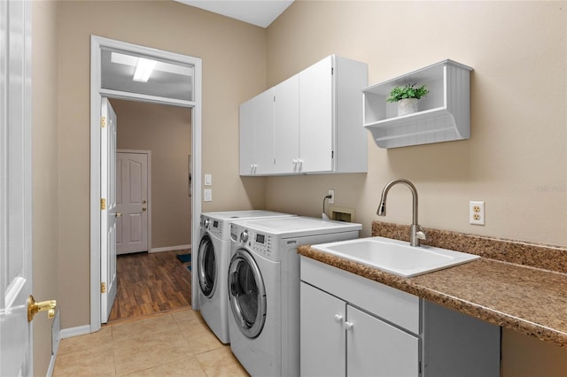 clothes washing area featuring sink, washing machine and dryer, light tile patterned floors, and cabinets