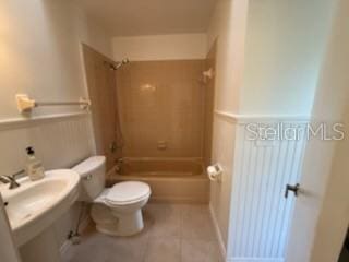 bathroom featuring a wainscoted wall, shower / bathing tub combination, toilet, and tile patterned floors