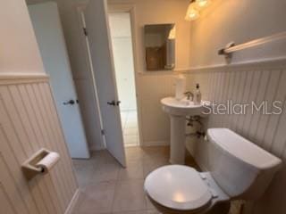 half bath featuring tile patterned flooring, a wainscoted wall, and toilet