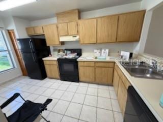 kitchen featuring light brown cabinets, under cabinet range hood, a sink, light countertops, and black appliances