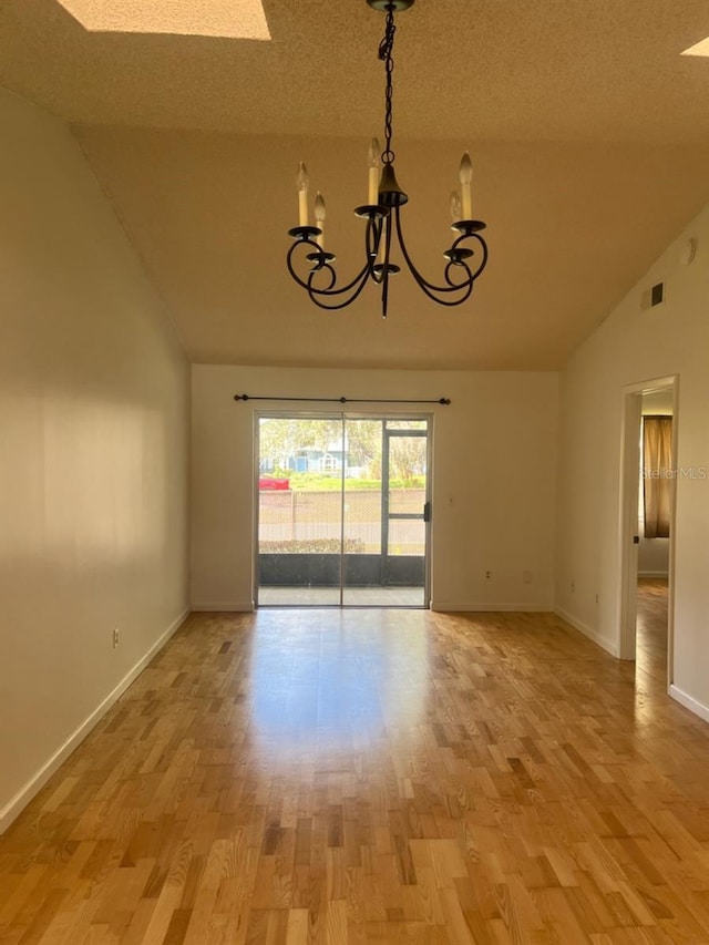 spare room featuring light wood-type flooring, a notable chandelier, vaulted ceiling, and baseboards