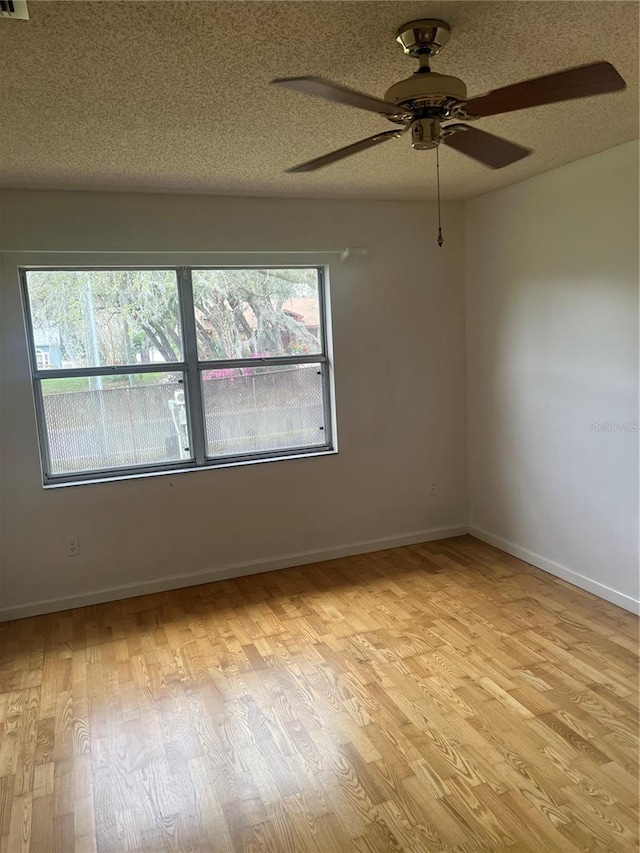 empty room with light wood finished floors, baseboards, a wealth of natural light, and a textured ceiling