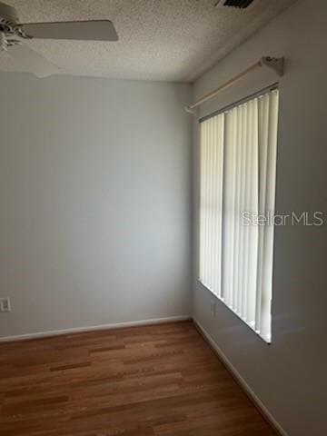 unfurnished room with a ceiling fan, a textured ceiling, baseboards, and wood finished floors